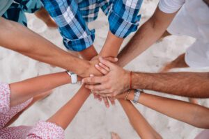 Group of diverse hands stacked together in a circle on a sandy beach, symbolizing teamwork and unity.