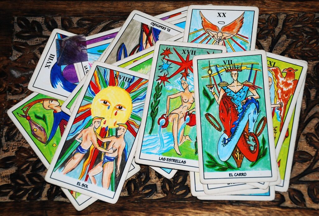 Tarot cards with bright illustrations scattered across a dark wooden table, showing suns, stars, and chariots among others.