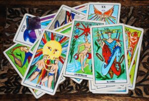 Tarot cards with bright illustrations scattered across a dark wooden table, showing suns, stars, and chariots among others.