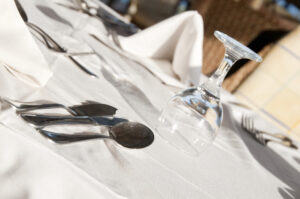Formal dining table setting with silverware laid out and an inverted wine glass on a white cloth tablecloth.