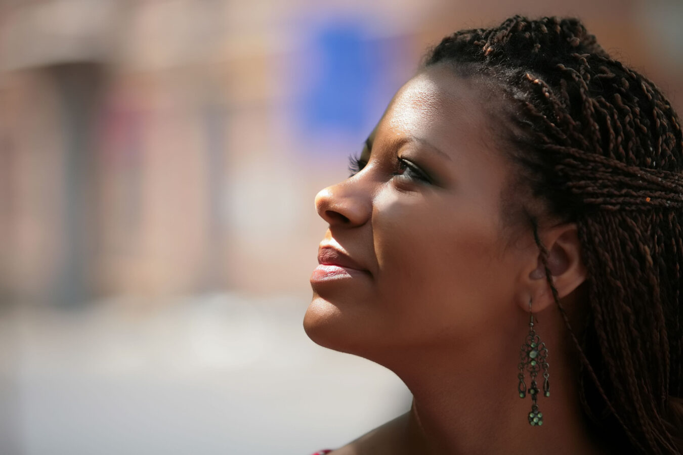 Close-up profile of a woman with braided hair wearing ornate green earrings, looking upward outdoors.
