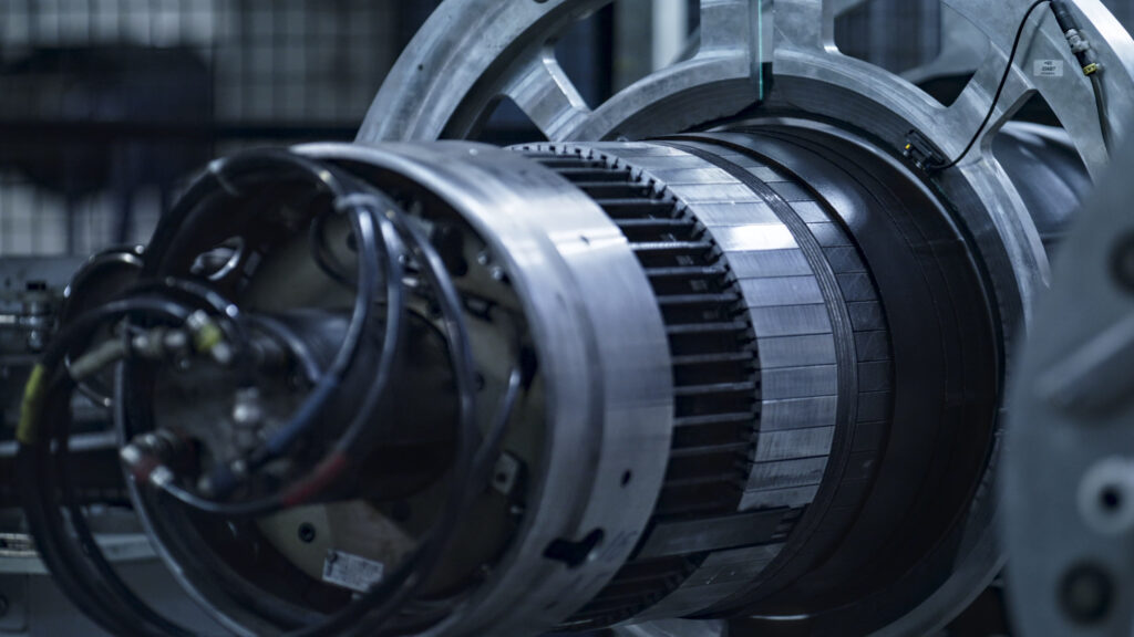 Close-up of a large turbine rotor with metallic rings and cables in an engineering workshop, showing exposed blades and hardware.